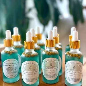 Puede incluir: Una colecci&oacute;n de botellas de aceite facial Skin & Soul Wellness. Cada botella de vidrio transparente tiene una tapa dorada y un cuentagotas blanco. El l&iacute;quido azul contiene peque&ntilde;os capullos de flores amarillas. La etiqueta dice "Skin Barrier Repair Facial Oil."