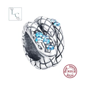 Op de afbeelding: Een zilveren bedel in de vorm van een opgerolde slang met een gestructureerd schubbenpatroon. De kop en het lichaam van de slang zijn geaccentueerd met kleine, ronde, felblauwe stenen. Een ronde stempel op de bedel vermeldt Real Sterling 925 Silver.