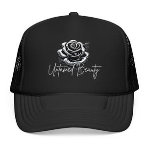May include: Black trucker hat with a mesh back and a curved brim. The front of the hat features a detailed grayscale rose graphic and the words "Untamed Beauty" in a cursive font. The hat is a classic accessory.