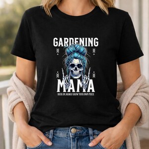 Pu&ograve; includere: T-shirt nero con grafica a teschio con occhiali da sole e chignon blu. Il testo recita "GARDENING MAMA" con "Rock on Mama! Grow your own piece" sotto. Il design ha un tema rock and roll.