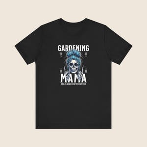 Pu&ograve; includere: T-shirt nera con una grafica raffigurante un teschio con capelli blu e occhiali da sole. Il testo recita "GARDENING MAMA" sopra e "MAMA" sotto il teschio, con "ROCK ON MAMA! GROW YOUR OWN PIECE" in basso.