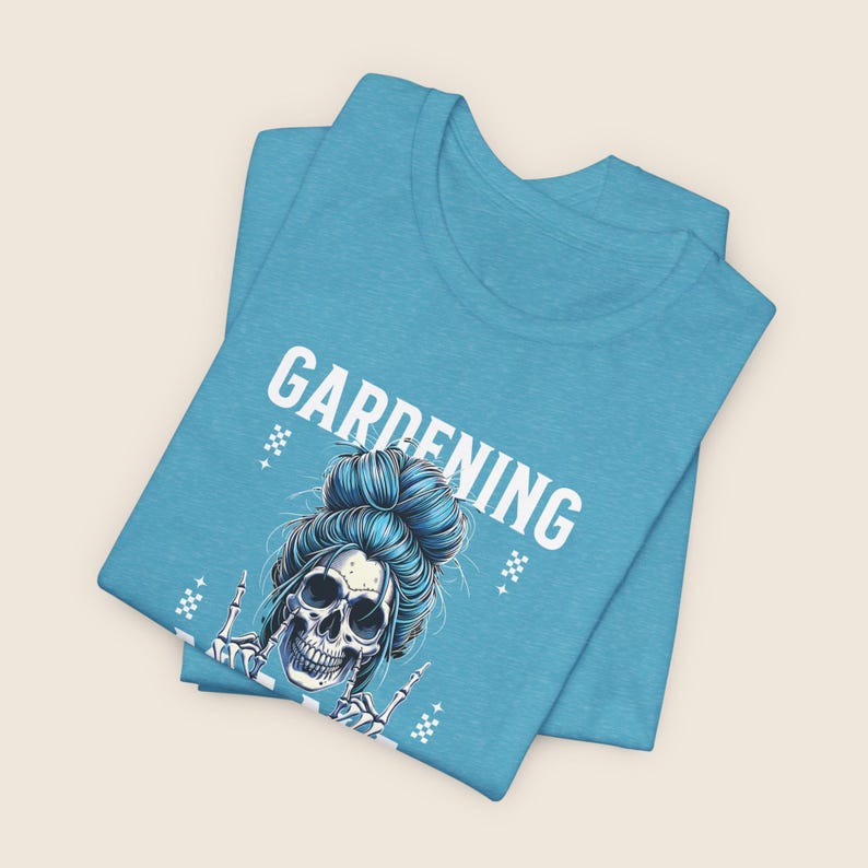Pu&ograve; includere: T-shirt azzurra con la scritta bianca "GARDENING". La grafica presenta un teschio con capelli blu raccolti in uno chignon e mani scheletriche che fanno un gesto rock. La maglietta &egrave; piegata.