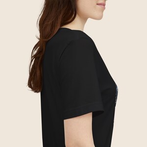Pu&ograve; includere: T-shirt nero a maniche corte. La maglietta ha uno scollo tondo ed &egrave; realizzata in un materiale morbido. L'immagine mostra la vista laterale della maglietta su una persona.