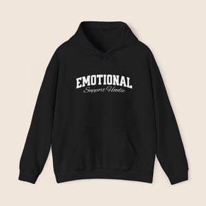 May include: Black hoodie with a front pocket and drawstring hood. The white text on the front reads "EMOTIONAL Support Hoodie". The hoodie is made of a soft material.