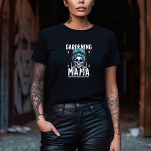 Pu&ograve; includere: T-shirt nera con la scritta "GARDENING MAMA" sopra una grafica a teschio con capelli blu e un gesto della mano. Il testo "ROCK ON MAMA GROW YOUR OWN PIECE" &egrave; sotto la grafica. La maglietta &egrave; girocollo.