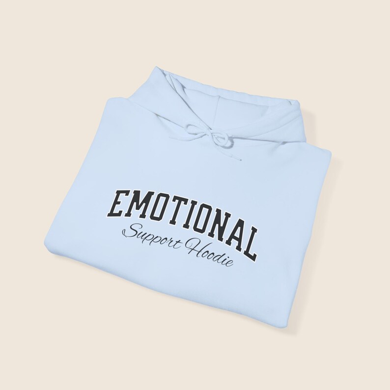 May include: A light blue hoodie with the words "EMOTIONAL" arched across the top and "Support Hoodie" below in a script font. The hoodie has a drawstring hood and is folded neatly.