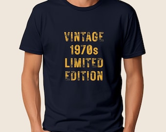 May include: Navy blue t-shirt with the words "VINTAGE 1970s LIMITED EDITION" in distressed yellow lettering. The text is stacked vertically. The shirt is a classic crew neck style.