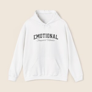 May include: A white hoodie with a front pocket and a drawstring hood. The text "EMOTIONAL" is printed above "Support Hoodie" in a black, stylized font.