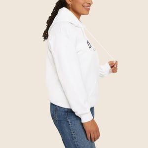 May include: A white hoodie with a drawstring and a front pocket. The hoodie has the word "ELEVATE" printed in black on the front. The person in the image is wearing blue jeans.