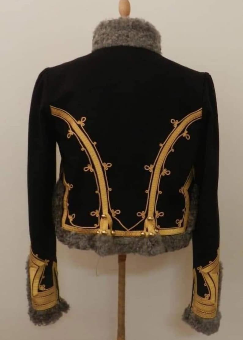 May include: Black jacket with gold trim and gray fur collar and cuffs. The jacket has gold decorative trim along the front and back. The jacket is displayed on a wooden stand. The jacket is a vintage style.