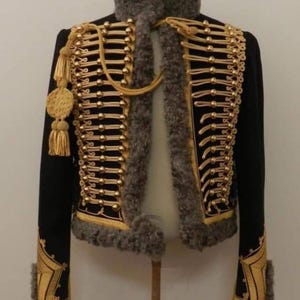 May include: Black jacket with gold trim and accents, featuring a high collar and decorative gold buttons. The jacket has a faux fur collar and cuffs, and gold embroidery on the sleeves. A tassel hangs from the left shoulder.
