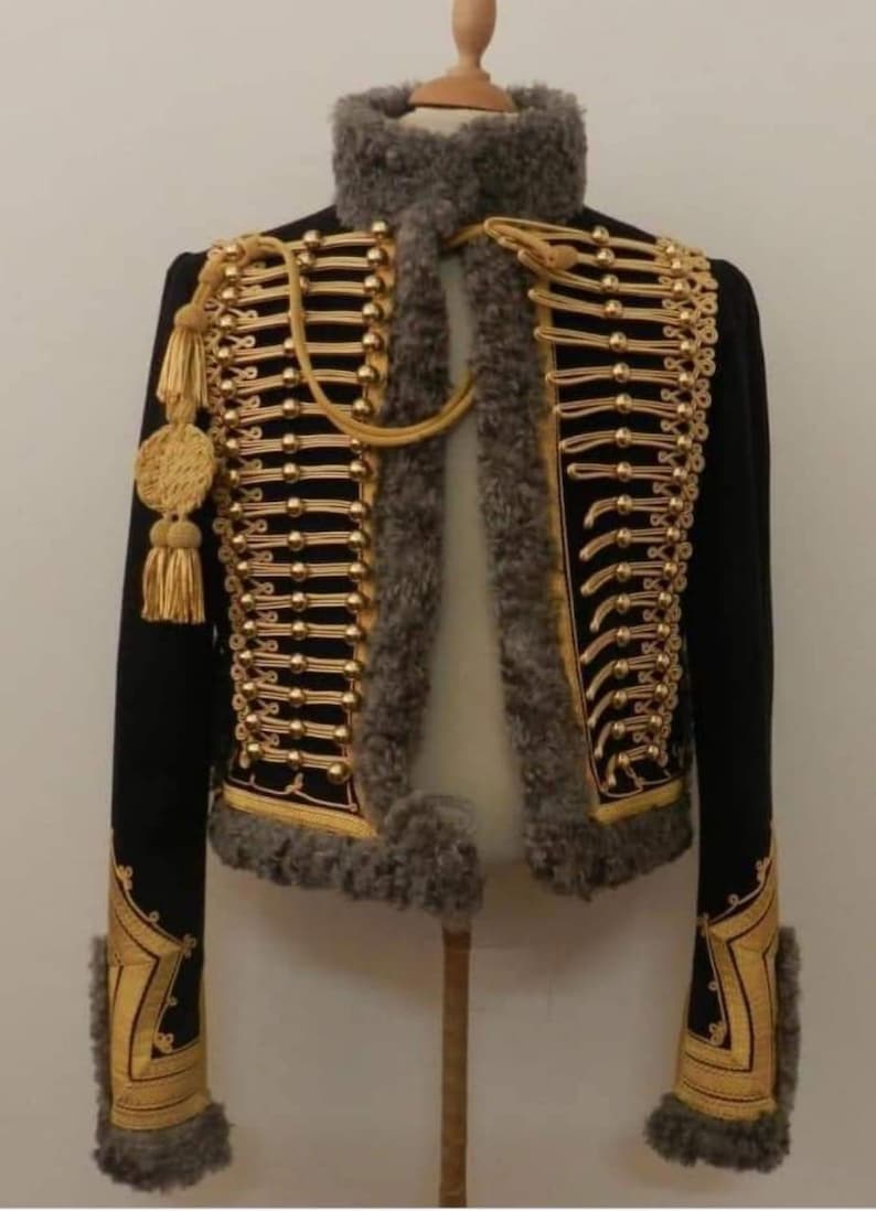 May include: Black jacket with gold trim and accents, featuring a high collar and decorative gold buttons. The jacket has a faux fur collar and cuffs, and gold embroidery on the sleeves. A tassel hangs from the left shoulder.