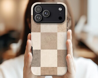 May include: A smartphone case with a neutral-toned, checkered pattern in shades of beige and brown. The case features a camera module with multiple lenses and a flash. The phone case is held in front of a blurred background.