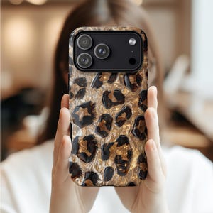 Puede incluir: Funda de teléfono con un diseño de estampado de leopardo dorado y negro. La funda tiene un acabado brillante y un módulo de cámara negro. El patrón de leopardo está detallado con manchas marrones oscuras y negras.