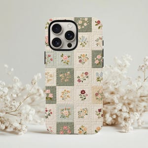 May include: A phone case featuring a patchwork design with embroidered floral patterns in pink, red, and yellow on a cream and green background. The case has a protective design with camera cutouts.