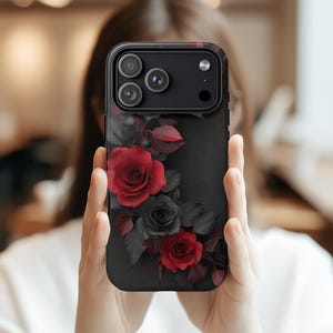 May include: Black phone case featuring a floral design with red and gray roses. The case has a matte finish and a camera cutout. The roses are arranged in a cluster, with detailed petals and leaves.