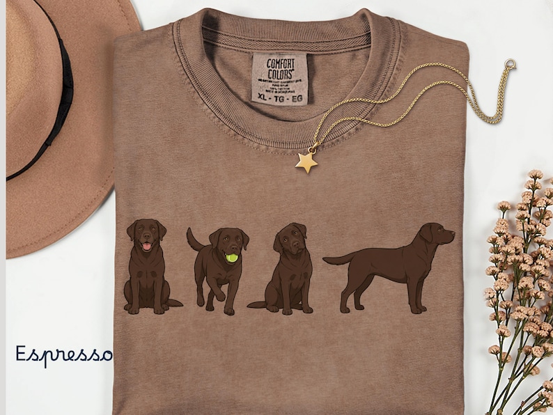 K&ouml;nnte beinhalten: Ein espressofarbenes T-Shirt mit einem Grafikdruck von vier schokoladenbraunen Labrador-Retrievern in verschiedenen Posen. Das Shirt hat einen Rundhalsausschnitt und ein Comfort Colors Markenetikett am Innenkragen mit der Gr&ouml;&szlig;enangabe XL.