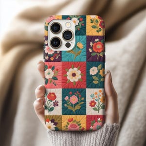 May include: A colorful phone case featuring a patchwork design with floral patterns. The case has a quilted appearance with squares of various colors, including red, teal, yellow, and purple. Each square showcases a different flower design.