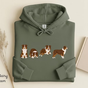 Könnte beinhalten: Ein militärgrüner Kapuzenpullover mit einem Grafikdruck von vier Australian Shepherd Hunden in verschiedenen Posen. Der Hoodie verfügt über eine Kapuze mit Kordelzug, lange Ärmel mit gerippten Bündchen und eine Kängurutasche auf der Vorderseite.
