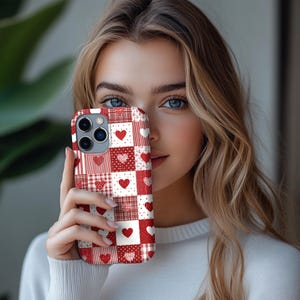 May include: A red and white patchwork phone case with heart patterns. The case features solid hearts, dotted hearts, and plaid squares. The case is designed for a smartphone with multiple camera lenses.