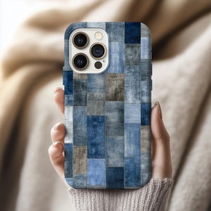 May include: A smartphone case featuring a patchwork design in various shades of blue, grey, and beige. The case is rectangular with rounded corners and a camera aperture. The design mimics a fabric quilt.