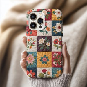 Può includere: Custodia per telefono colorata con un design patchwork floreale. Tenuta in mano, mostra quadrati con illustrazioni floreali variegate in tonalità di rosso, giallo e blu, creando un effetto visivo vivace.