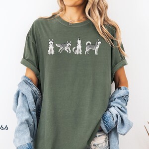 May include: Moss green t-shirt featuring a line of embroidered Siberian Husky dogs in various poses. The shirt has short sleeves and a relaxed fit. The word "Moss" is printed in the lower left corner.