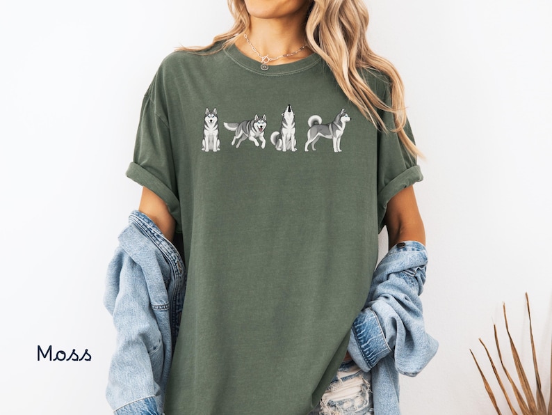 May include: Moss green t-shirt featuring a line of embroidered Siberian Husky dogs in various poses. The shirt has short sleeves and a relaxed fit. The word "Moss" is printed in the lower left corner.