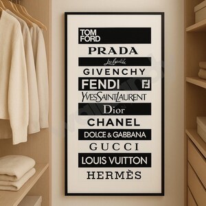 May include: A framed black and white print displaying the logos of high-end fashion brands including Tom Ford, Prada, Givenchy, Fendi, Yves Saint Laurent, Dior, Chanel, Dolce & Gabbana, Gucci, Louis Vuitton, and Herm&egrave;s. The print is in a wardrobe.
