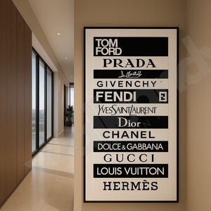 May include: A framed black and white art print displaying the logos of high-end fashion brands including Tom Ford, Prada, Givenchy, Fendi, Dior, Chanel, and Louis Vuitton. The print hangs on a beige wall in a hallway.