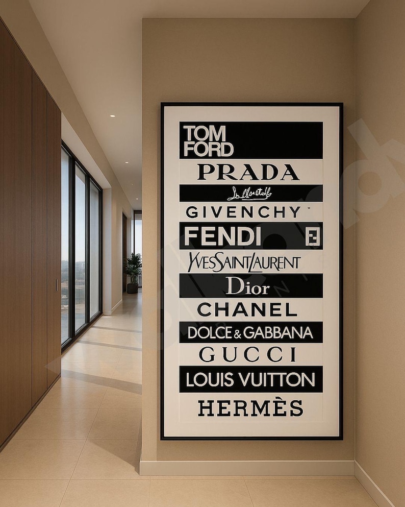 May include: A framed black and white art print displaying the logos of high-end fashion brands including Tom Ford, Prada, Givenchy, Fendi, Dior, Chanel, and Louis Vuitton. The print hangs on a beige wall in a hallway.