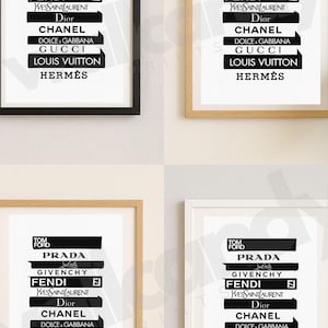 May include: Four framed prints with a minimalist design featuring luxury brand logos in black and white. The brands include Prada, Chanel, Gucci, and others. Each print is in a different coloured frame: black, gold, and white.