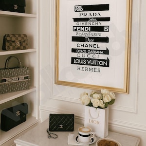 May include: A gold-framed print displaying luxury brand logos such as Prada and Chanel. A Dior shopping bag with white roses sits on a marble surface. A black quilted leather handbag and coffee with biscuits are also present. Designer handbags are on a shelf.