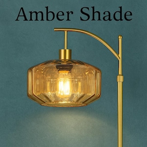 K&ouml;nnte beinhalten: Eine Stehlampe mit einem goldfarbenen Metallst&auml;nder und einem breiten, facettierten Glasschirm in Bernstein. Die Lampe verf&uuml;gt &uuml;ber einen gebogenen Arm und eine leuchtende Gl&uuml;hbirne im Glas. Der Text Amber Shade steht oben im Bild in schwarzer Schrift.