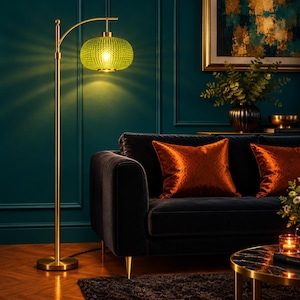 May include: A tall floor lamp with a slender gold-toned metal stand and a circular base. The lamp features a rounded, textured lime green glass shade that emits a warm, glowing light, suspended from a curved arm at the top of the pole.