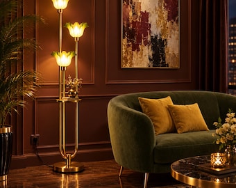 May include: A floor lamp with a gold-toned metal frame and three flower-shaped glass shades in a light green hue. The lamp features a small circular shelf integrated into the central pole, providing a surface for decorative items.