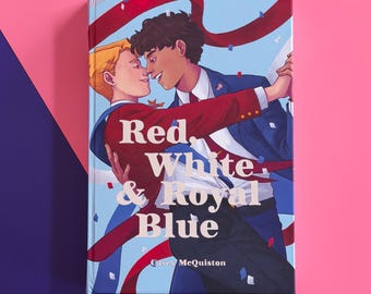 Może przedstawiać: Książka w twardej oprawie pod tytułem Red, White & Royal Blue autorstwa Casey McQuiston. Okładka przedstawia ilustrację dwóch osób tańczących na jasnoniebieskim tle z czerwonymi wstążkami i konfetti. Jedna osoba ma na sobie czerwoną marynarkę, druga niebieski garnitur.