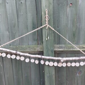 May include: A handmade advent calendar made from a natural branch and twine. Twenty small wooden discs, each numbered 1 to 20, are suspended from the branch. The background is a wooden fence.