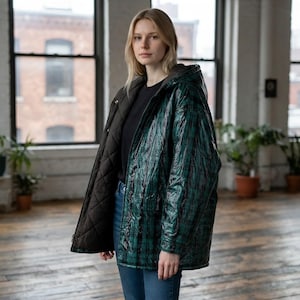 May include: A hooded jacket featuring a glossy green and black plaid exterior and a contrasting matte black quilted interior lining. The garment is worn open over a plain black shirt and blue denim jeans, showcasing the dual-textured design.