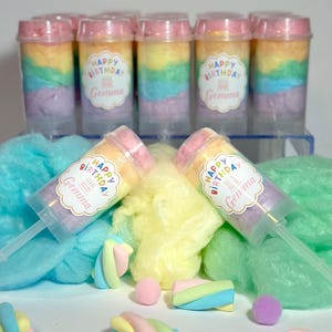 May include: Cotton candy push pops in rainbow colors with a pink lid. Each pop has a sticker that says "Happy Birthday Gemma". Marshmallows and cotton candy in pastel colors are scattered around the pops.