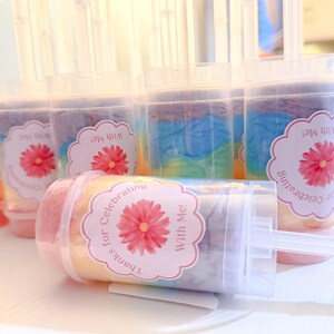May include: Clear push-pop containers filled with colorful, layered treats. Each container has a label with a pink flower and the text "Thanks for Celebrating With Me!". The treats inside have pastel colors.