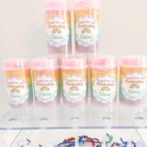 May include: A display of cotton candy party favors in clear plastic containers with pink lids. Each container has a rainbow of cotton candy and a sticker that says "Thank you for Celebrating Eliana's 5th Birthday With Us."