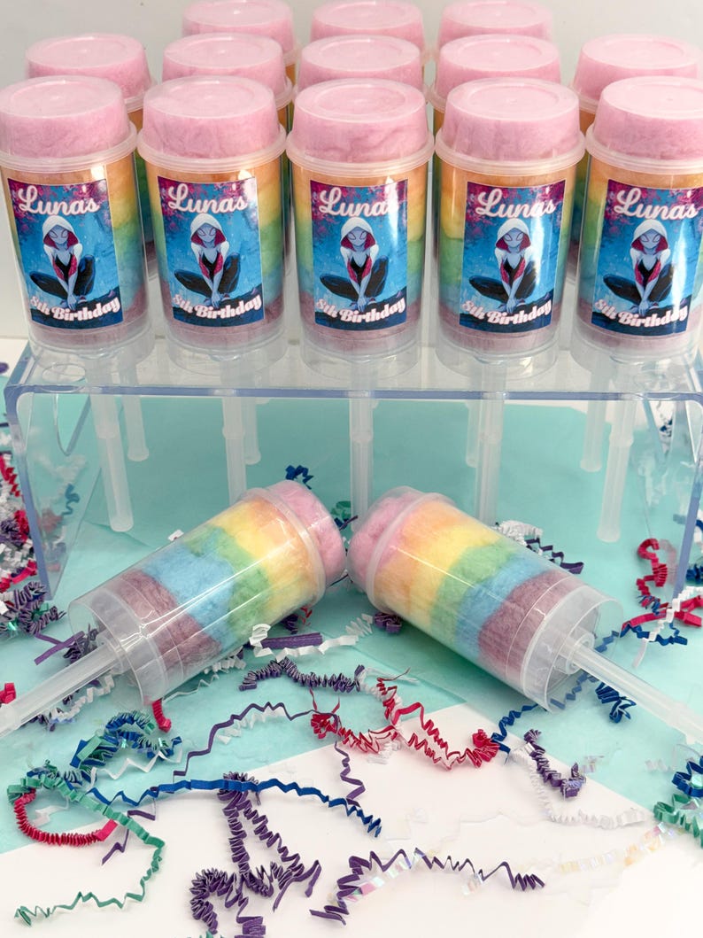 May include: Clear plastic push pop containers filled with rainbow-colored cotton candy. Each container has a pink lid and a label that reads "Luna's 8th Birthday" with a cartoon character. The containers are displayed on a clear plastic stand.
