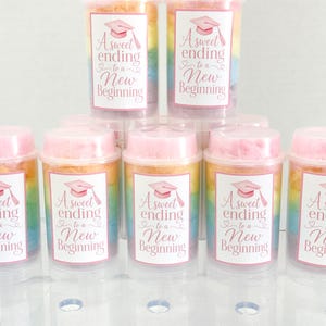 May include: Clear plastic containers filled with colorful cotton candy. Each container has a pink lid and a label with a graduation cap and the text "A sweet ending to a New Beginning."