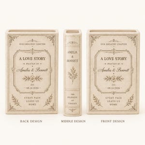 May include: A cream-colored ceramic book-shaped vase featuring black text and floral line art. The front and back display 'A LOVE STORY', 'Amelia & Bennett', and '08.16.2026'. The spine reads 'AMELIA & BENNETT' and 'THE BEGINNING OF FOREVER'.