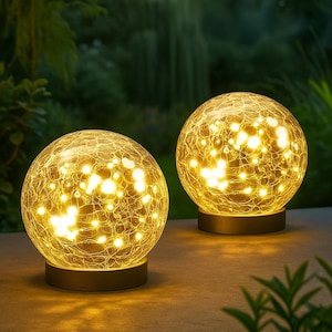 May include: Two illuminated, spherical outdoor lights. Each light has a cracked glass globe that emits a warm, yellow glow. The lights sit on a dark, circular base, creating a soft, ambient lighting effect for gardens or patios.