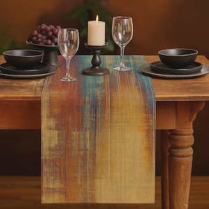 Może przedstawiać: Nakrycie stołu z kolorowym bieżnikiem. Bieżnik ma teksturowany wzór w odcieniach niebieskiego, pomarańczowego i żółtego. Stół jest nakryty czarnymi miskami, talerzami, kieliszkami do wina, zapaloną świecą i miską winogron.