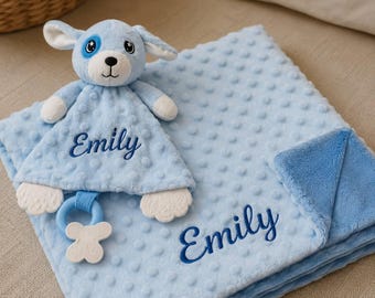 May include: A light blue baby security blanket and a matching plush dog toy, both featuring the name Emily embroidered in dark blue script. The blanket has a textured dimpled surface and a smooth blue underside, while the dog toy includes a white teether.