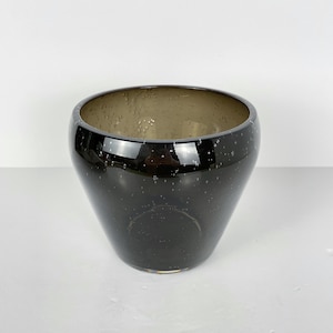 May include: A white ceramic mug with a black handle and the text "But First, Coffee" in a bold, black font. The mug is set against a blurred background, highlighting its simple design.