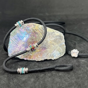 May include: Black dog leash and collar set with decorative rhinestone accents. The collar and leash are made of a durable black cord. The collar features a silver paw print charm. The collar and leash have silver and rhinestone accents.